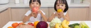 Two children are sitting in a kitchen. The boy is eating an apple, the girl is eating a yellow fruit. On the counter in front of them is a large selection of colourful fruit and vegetables. Lu and colleagues assessed dietary pesticide intake and potential health effects in children of school age.